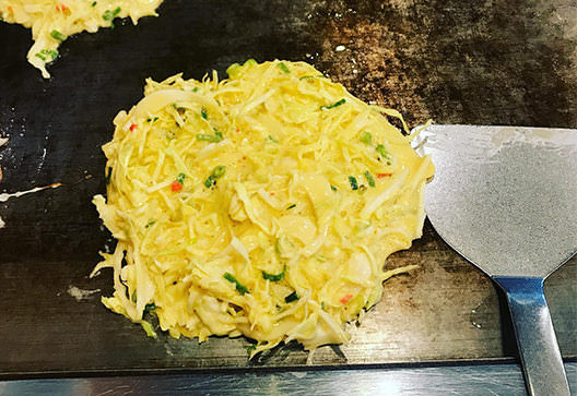 広島の月刊わしら：鉄板の上で焼かれるお好み焼き